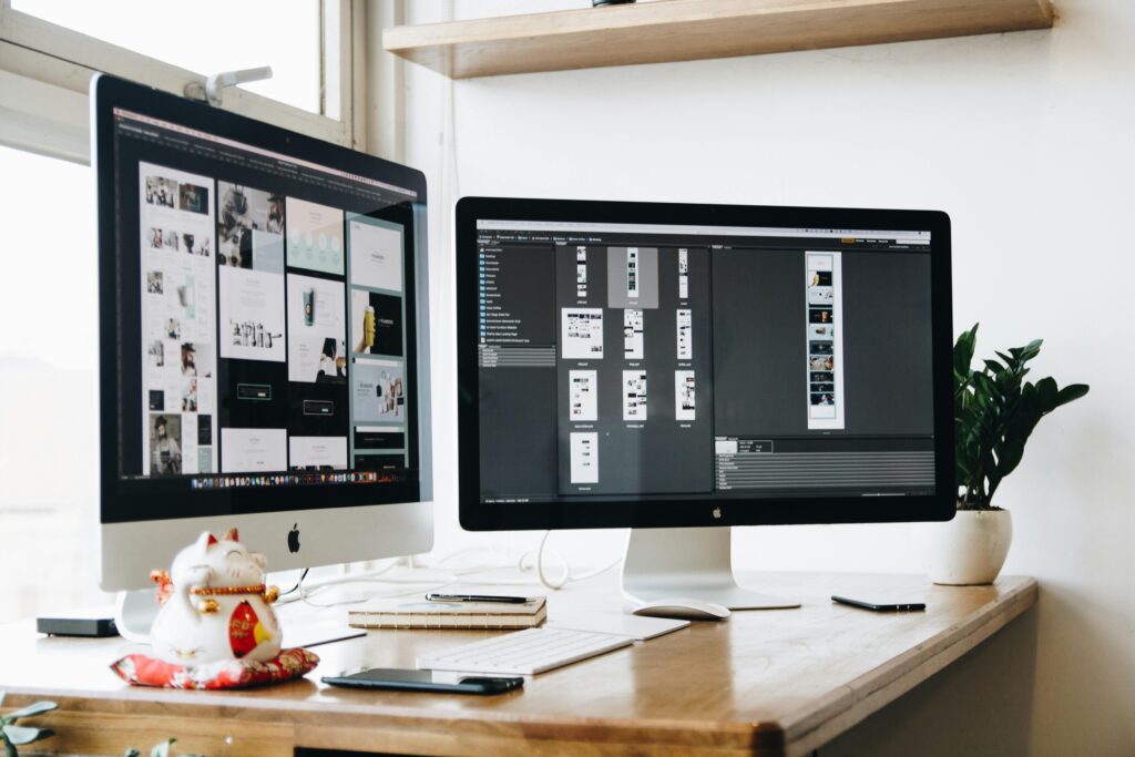 Computer monitors sitting on a desk displaying website designs on their screen